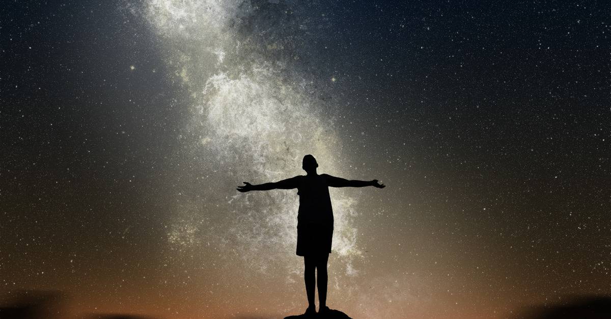 man standing on rock with open arms welcoming the light of night sky