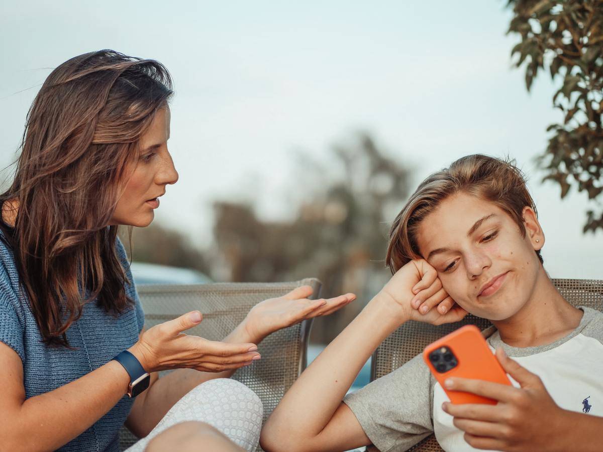 -boy-looking-at-his-smartphone-while-his-mother-is-talking