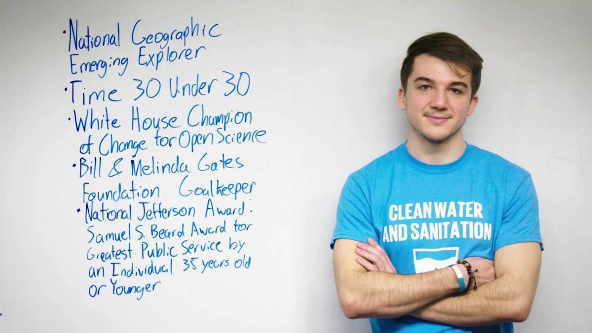 Jack poses beside white board that lists all of his accomplishments