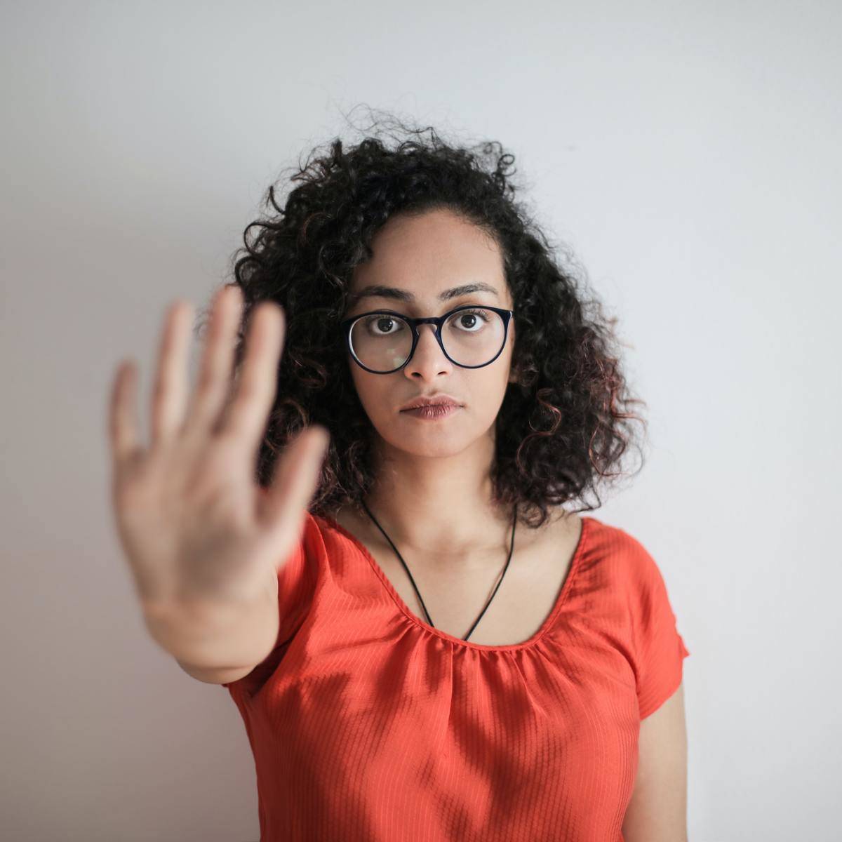 portrait-photo-of-woman-in-red-top-wearing-black-framed-eyeglasses-holding-out-her-hand-in-stop-gesture-