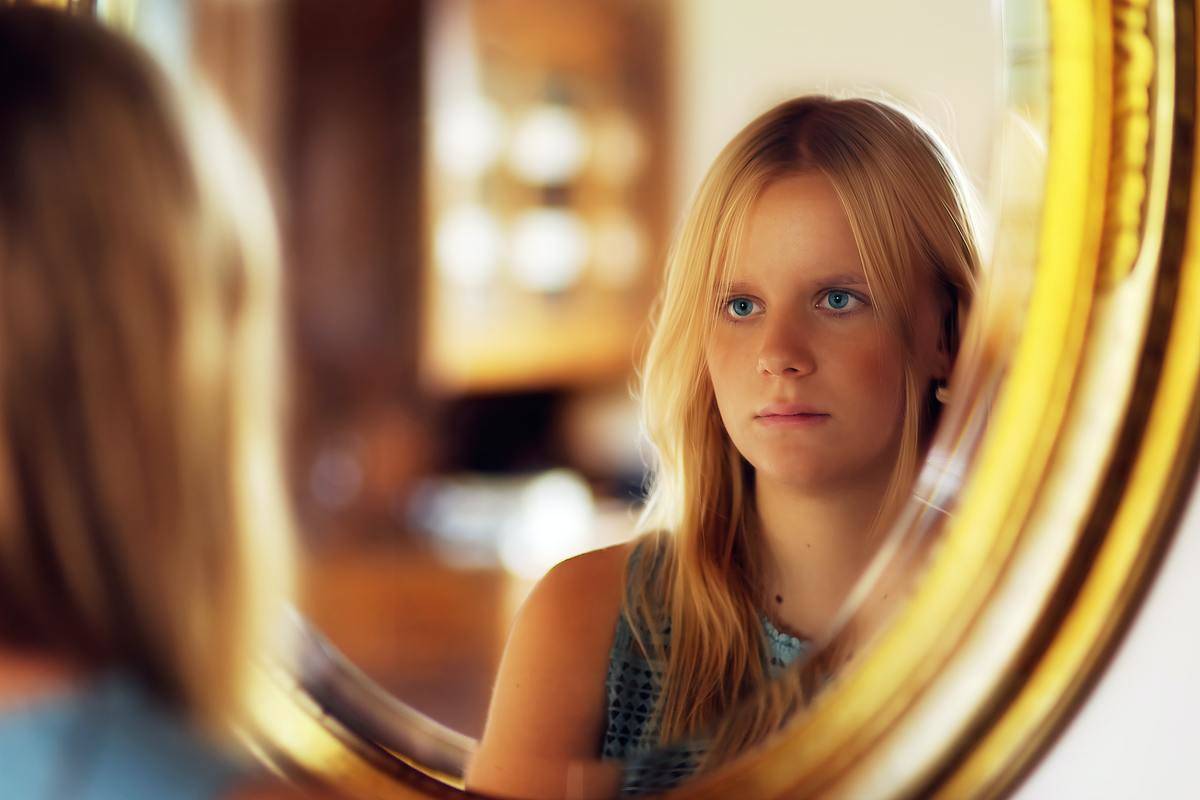 girl-in-black-and-white-polka-dot-sleeveless-shirt looking at herself in the mirror