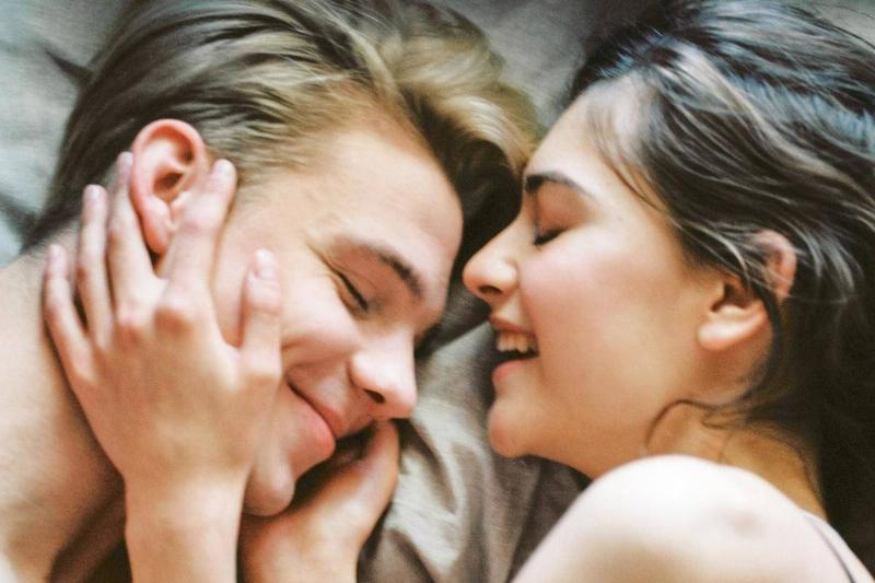 woman holds smiling man's face affectionately in bed