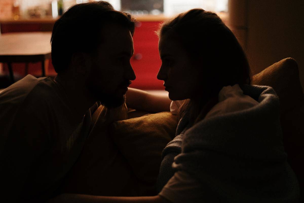 couple faces each other on the couch at home in dark lighting