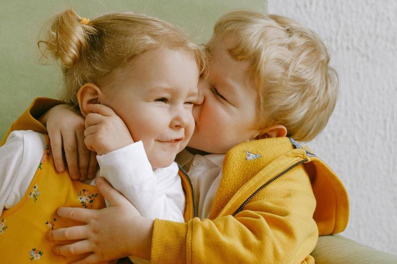 cheerful-little-siblings-hugging-in-armchair-at-home-