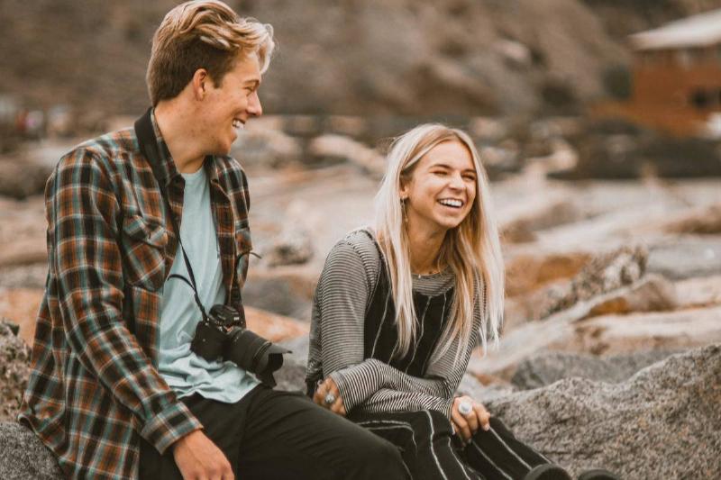 man-and-woman-sitting-on-a-rock laughing