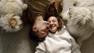 couple-lying-on-the-carpet-with-their-dog as he kisses her cheek