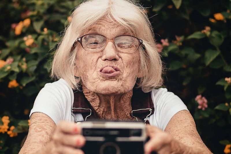 old woman taking-selfie with old camera and sticking her tongue out