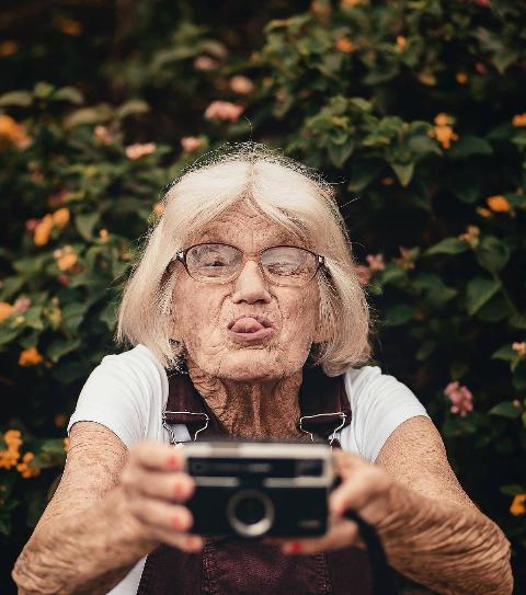 old woman taking-selfie with old camera and sticking her tongue out