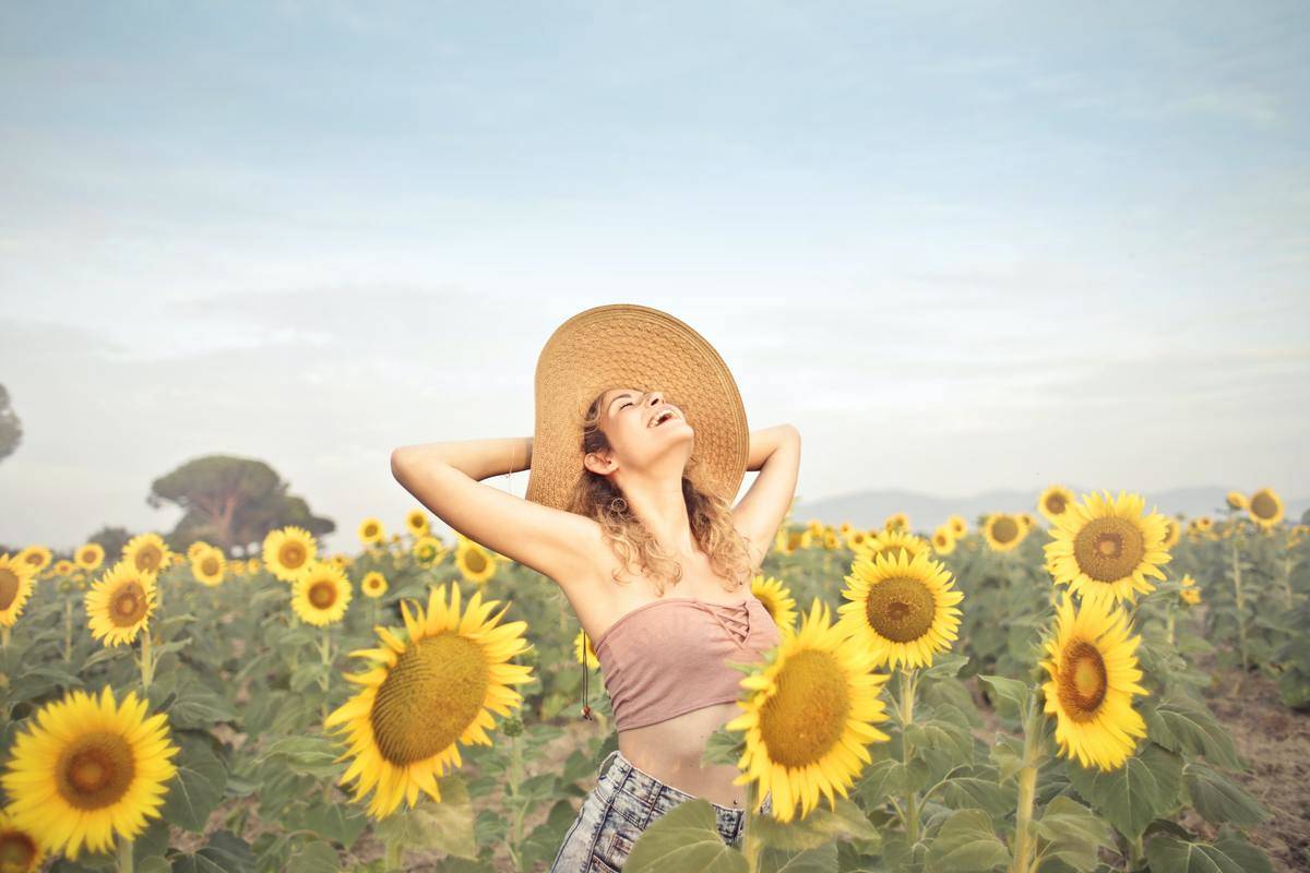 woman-standing-on-sunflower-field with hat smiling
