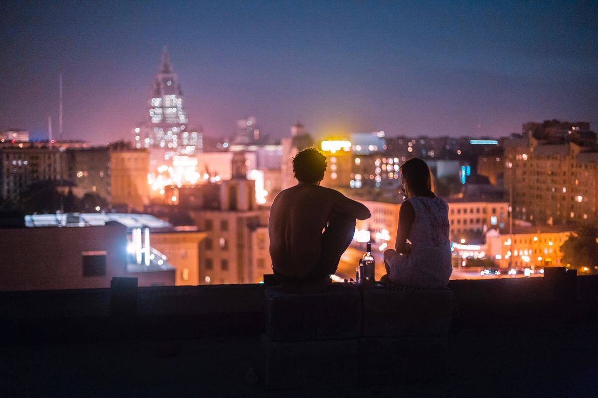 silhouette of couple sits on edge of building facing city lights