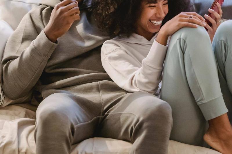 happy-black-couple-on-couch-with-smartphone- laughing