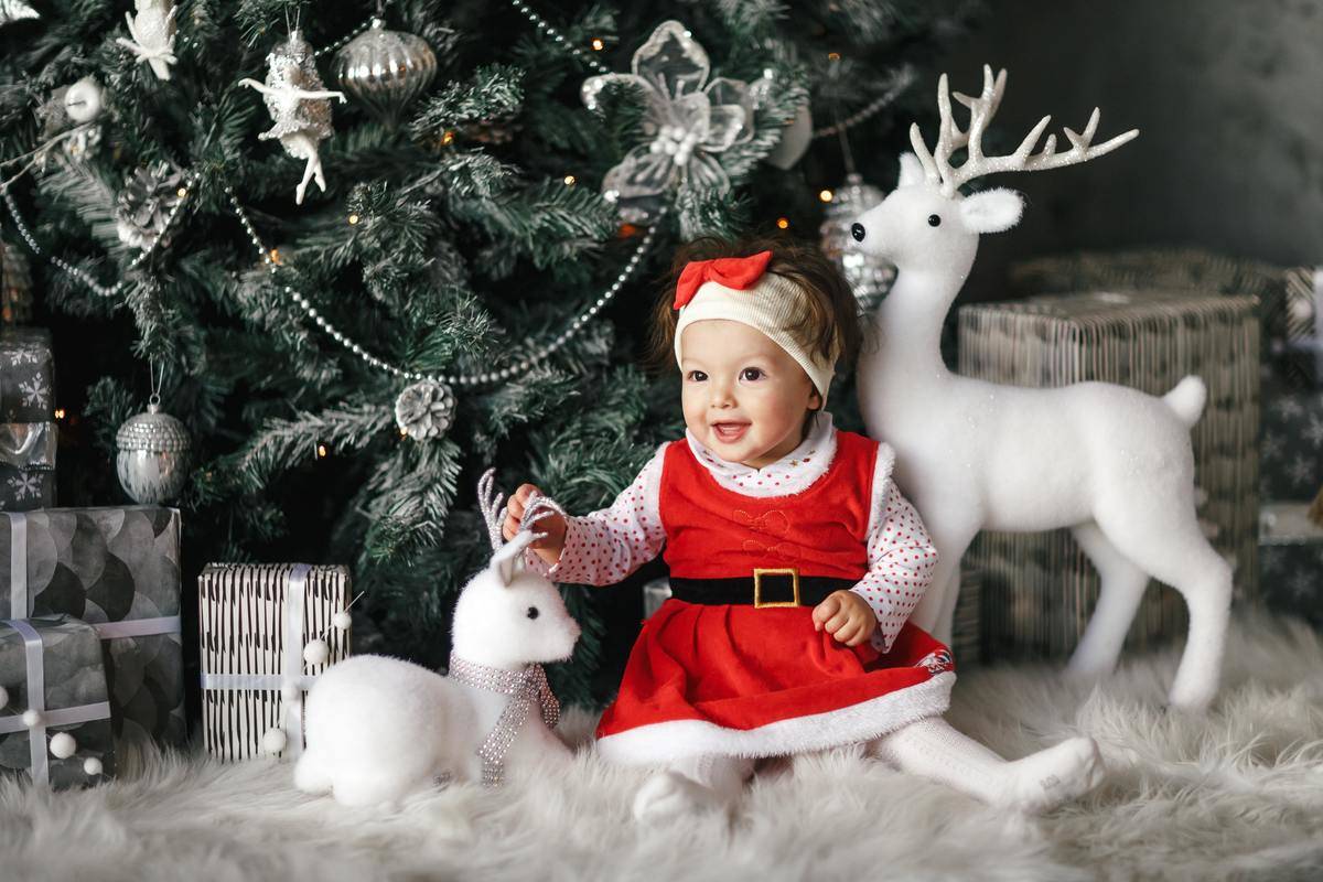 baby-girl-wearing-santa-dress-sitting-beside-christmas-tree