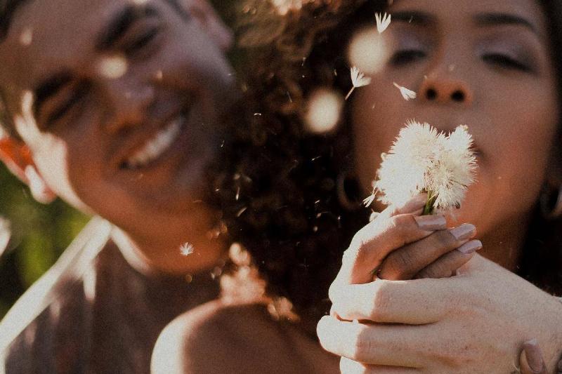 -woman-blowing-a-dandelion-flower- with man looking at her smiling