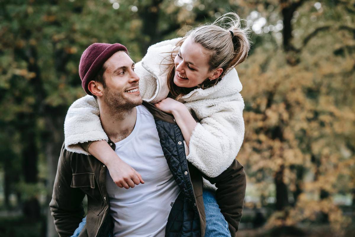 smiling-woman-on-back-of-boyfriend in forest