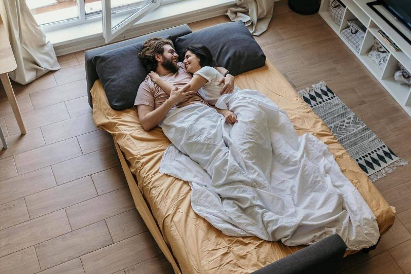 man-and-woman-lying-on-bed cuddling and smiling