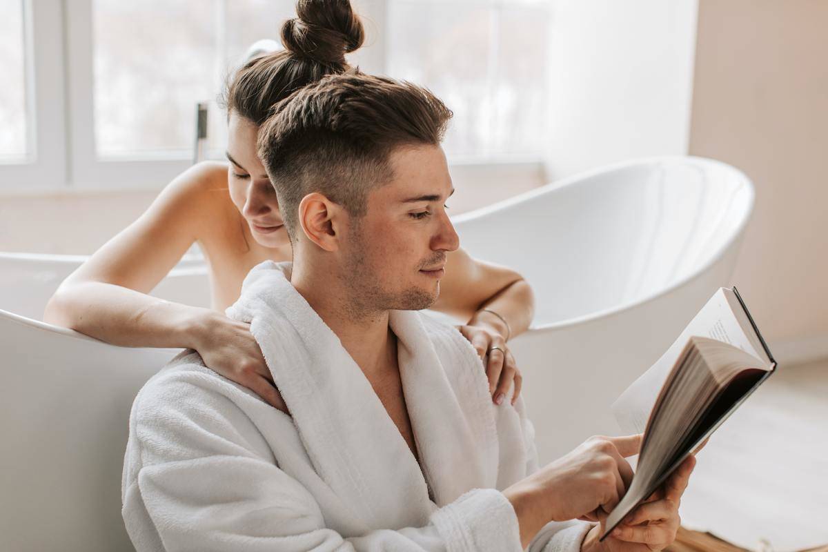 woman-hugging-her-husband from the bathtub while he reads