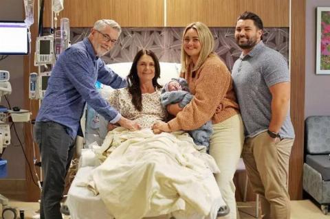 family at hospital bed smiling with baby