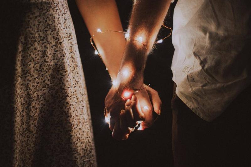 man-and-woman-holding-each-others-hand-wrapped-with-string-lights