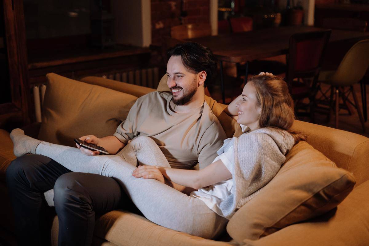 man-and-woman-sitting-on-couch cuddling with tv romote