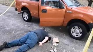 man plays dead by orange car
