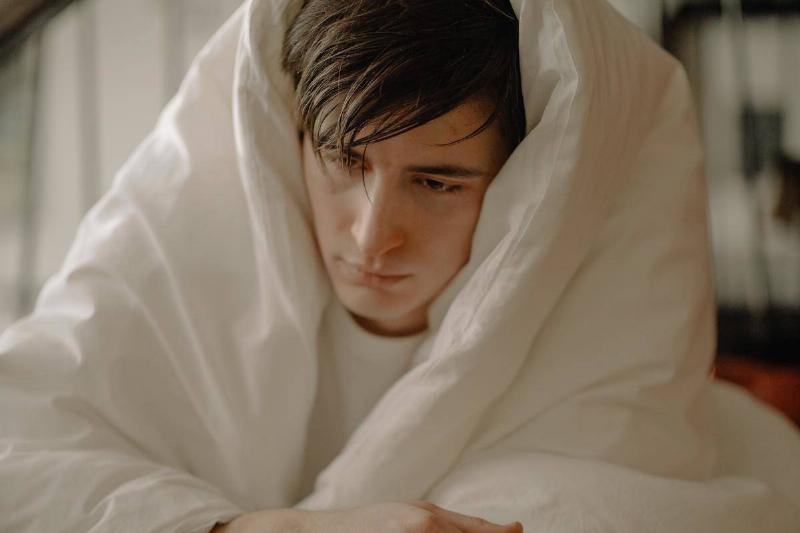 man wrapped in blanket looking miserable