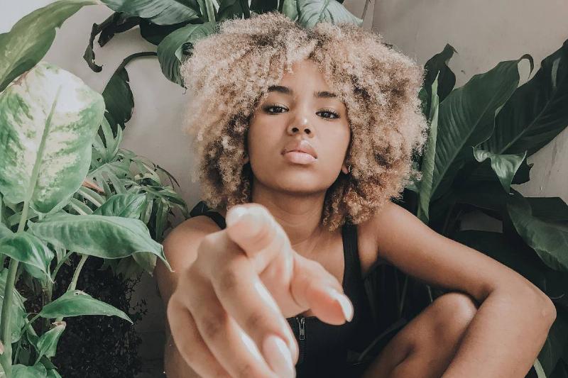 ensive-blonde Black woman-pointing-index-finger-at-camera-sitting with plants