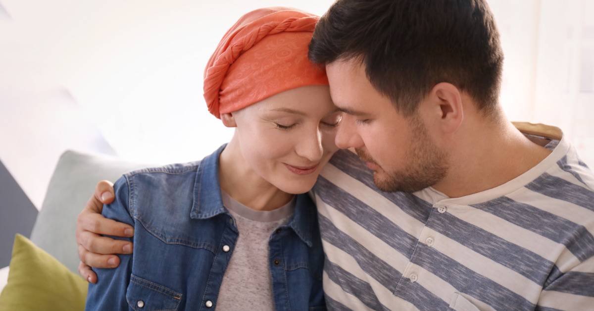 sick woman wearing head wrap comforted by man