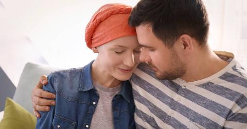 sick woman wearing head wrap comforted by man