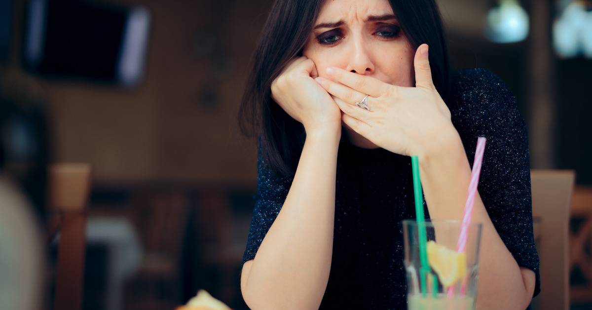 woman has hiccups at restaurant, holding her hand to her mouth