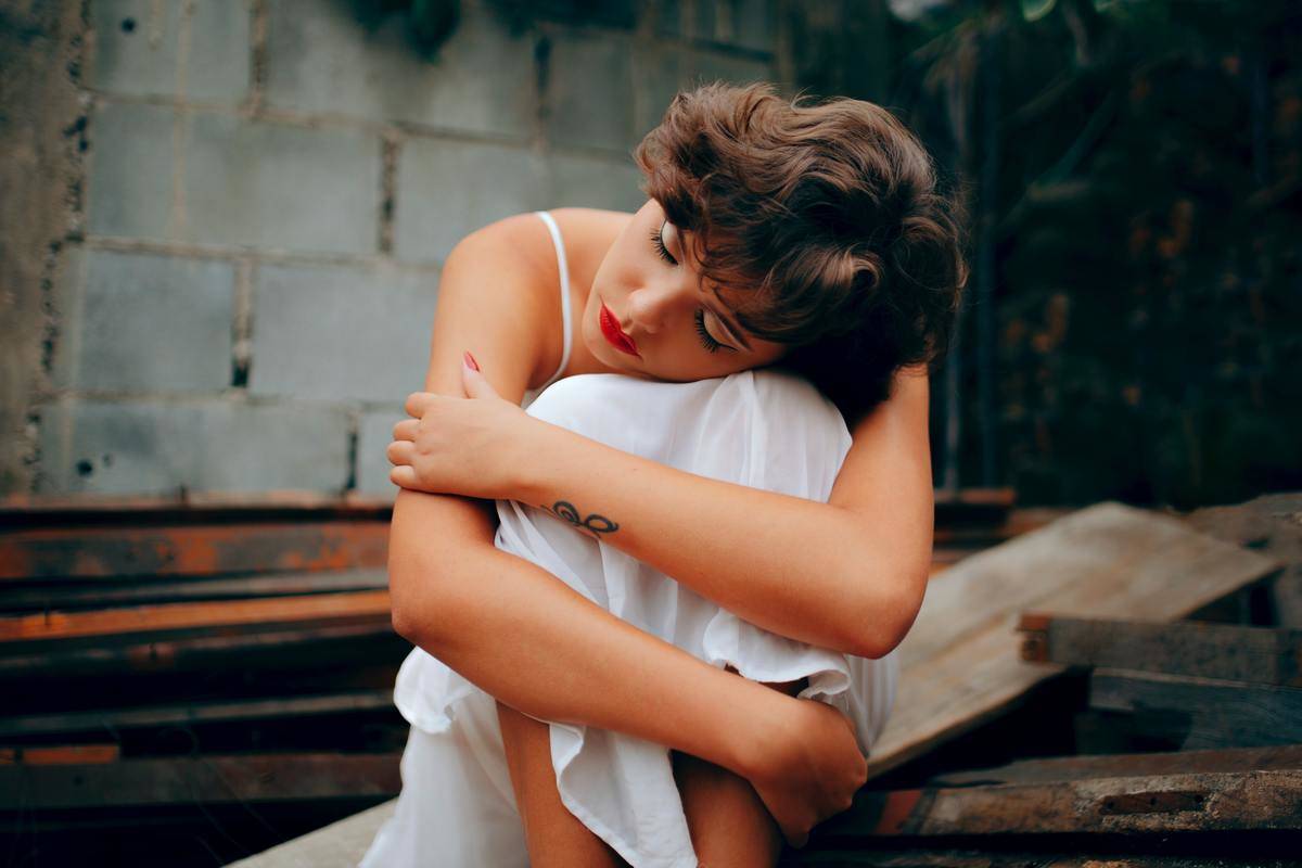 woman in white dress hugs in her knees sitting on the floor by bricks