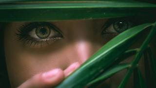 woman looking through leafs with green eyes