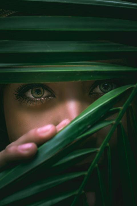 woman looking through leafs with green eyes