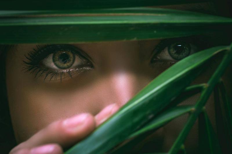 woman looking through leafs with green eyes