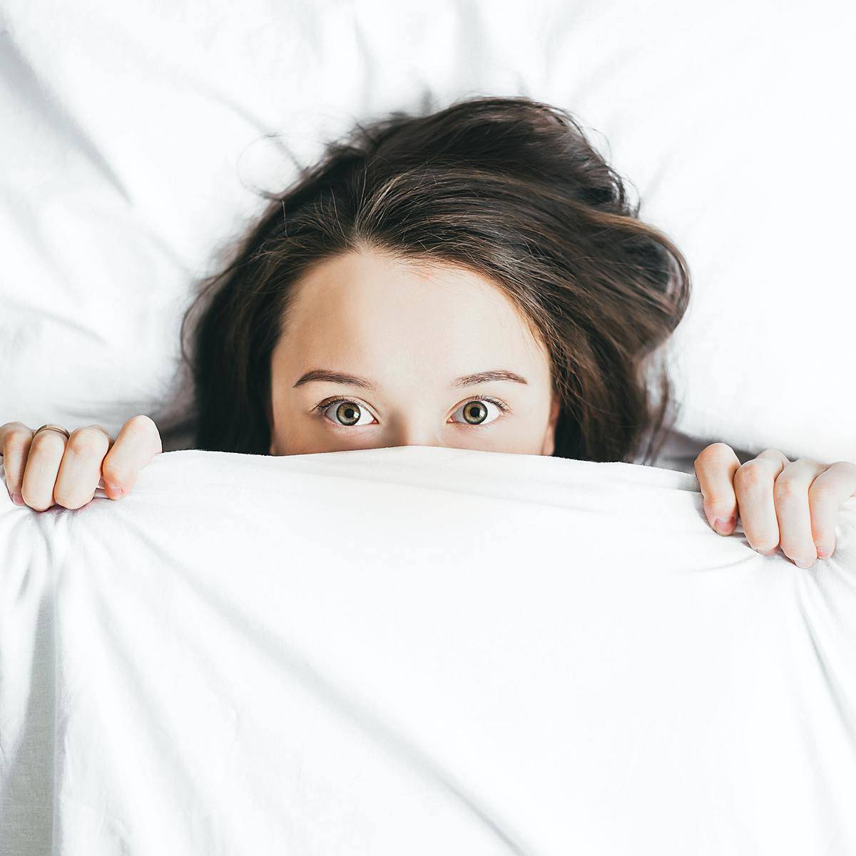 woman peeking from under the covers with green eyes