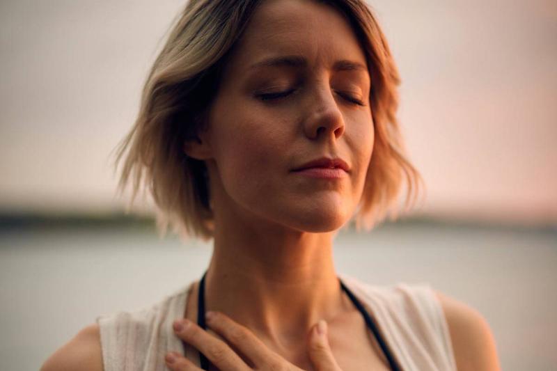 woman rests hand on her heart with eyes closed by beach 