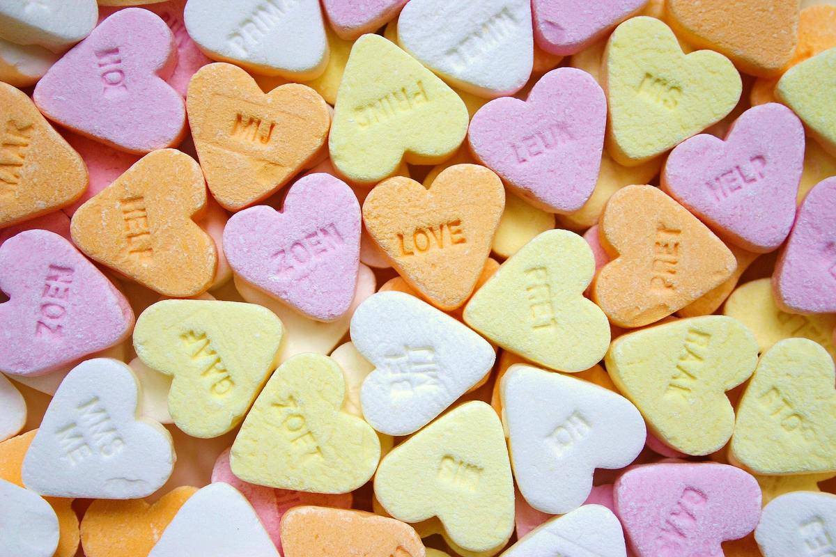 A number of bright candy hearts, one in the center has the word 'LOVE' stamped on it.