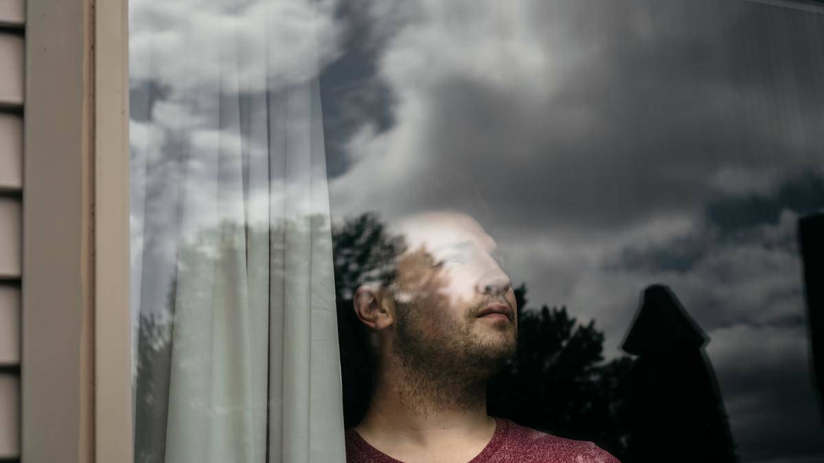 A man looking up into the distance through a window, in which we can see clouds reflected.
