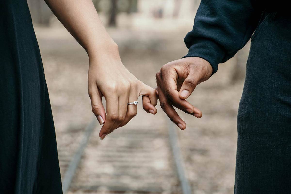 A closeup of a man and a woman with their pinkies interlocked, the woman sporting a ring.