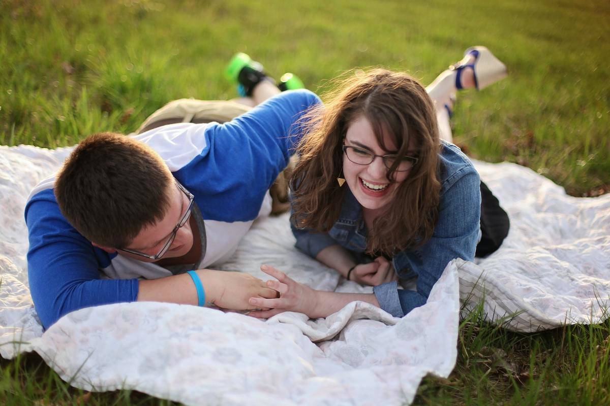 Two people laughing while laying on a blanket in the grass.