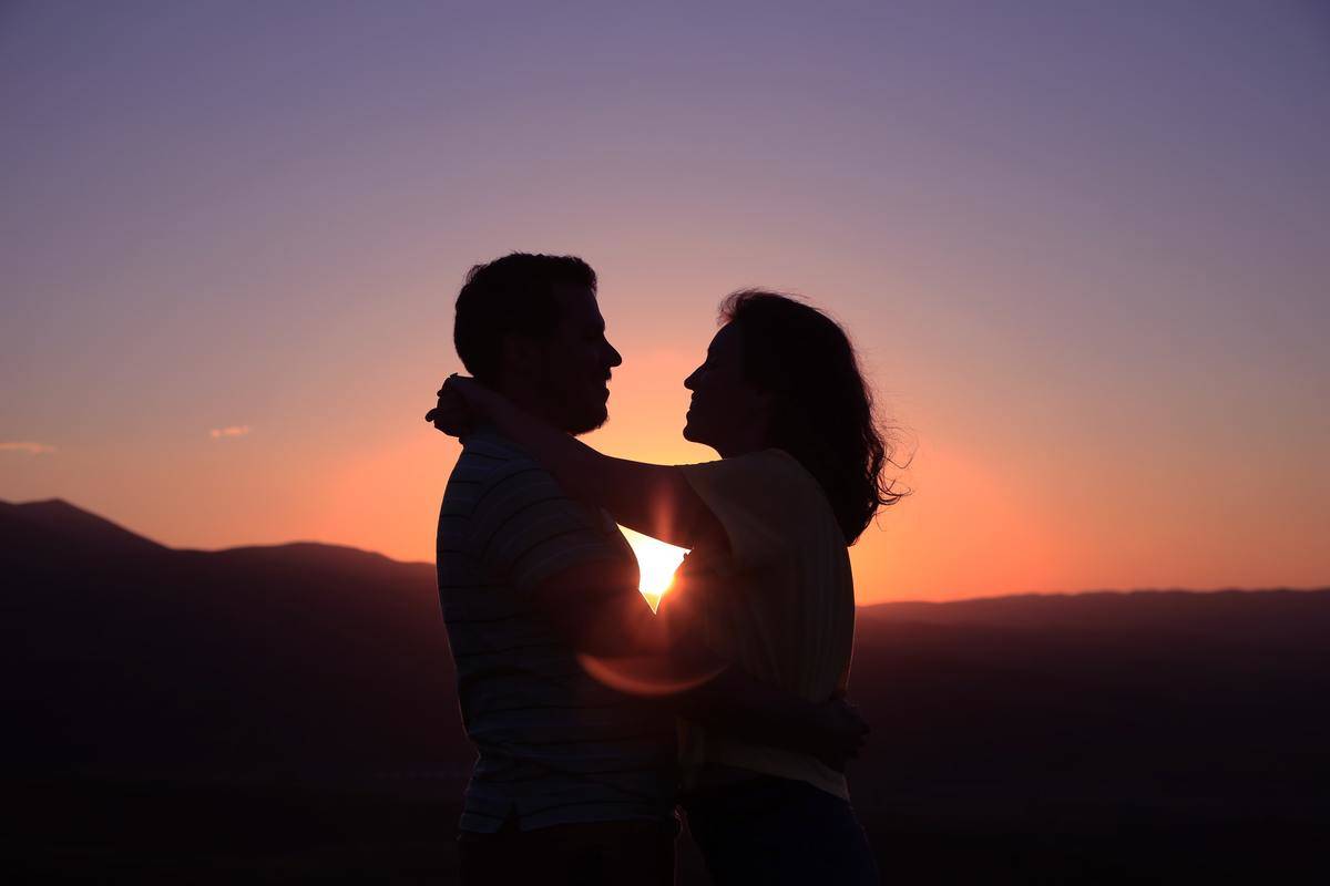 The silhouette of a couple embracing in front of a sunset.