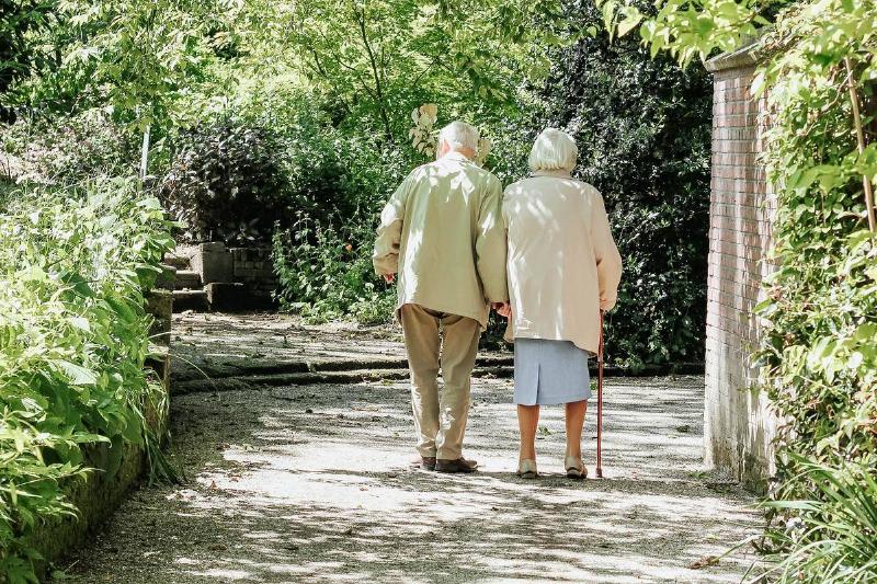 An elderly couple holding hands and walking down a path.