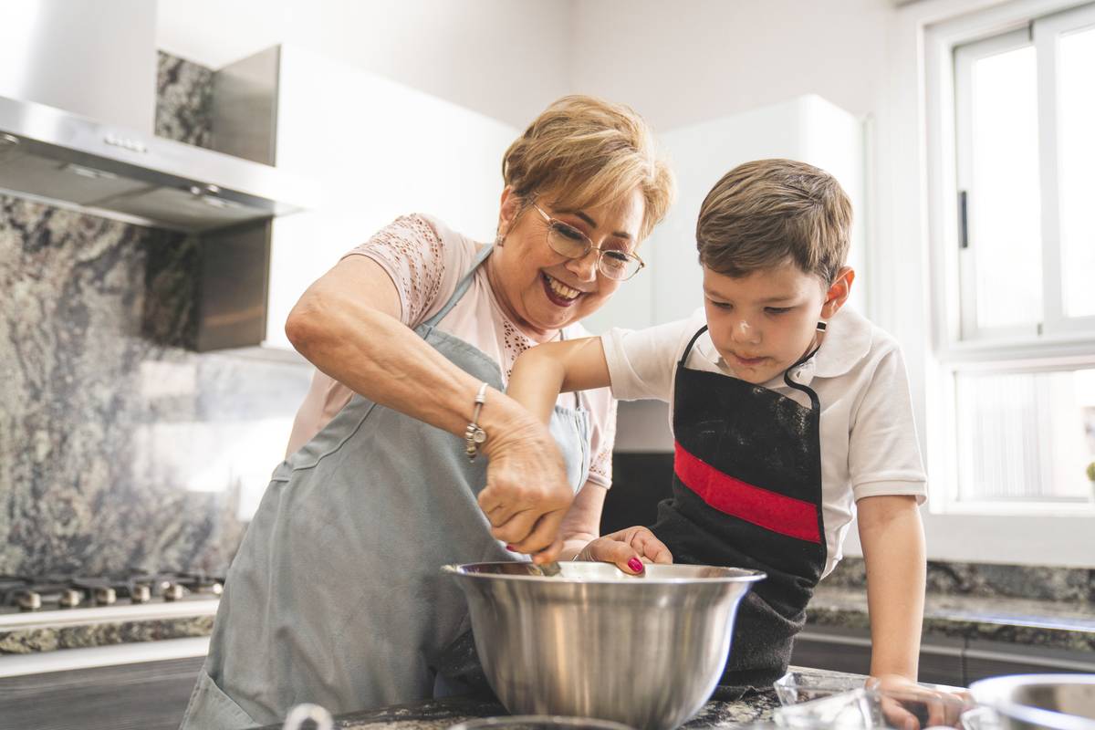 A young boy is mixing ingredients in a bowl alongside his grandmother.