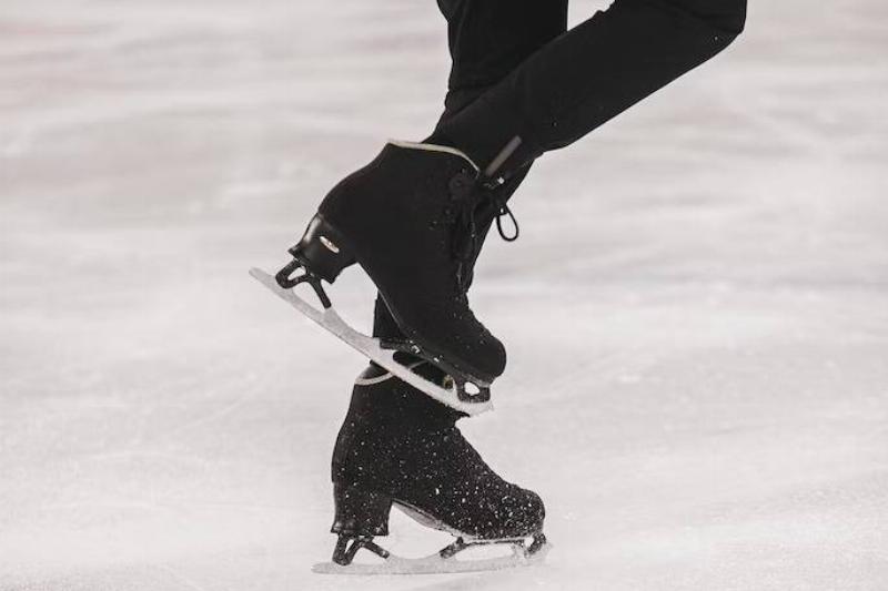 A closeup of a man's legs and skates as he figure skates.