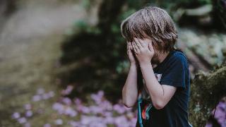 A young boy covering his face with his hands, appearing to be crying.