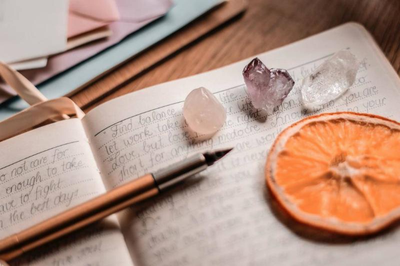 A page of a journal filled with writing. A pencil, some crystals, and a dried orange slice rests on top.