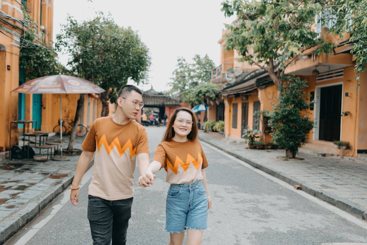 positive asian couple holding hands walking on city street