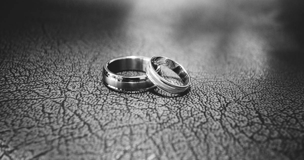 A closeup of two wedding rings atop leather, in greyscale.