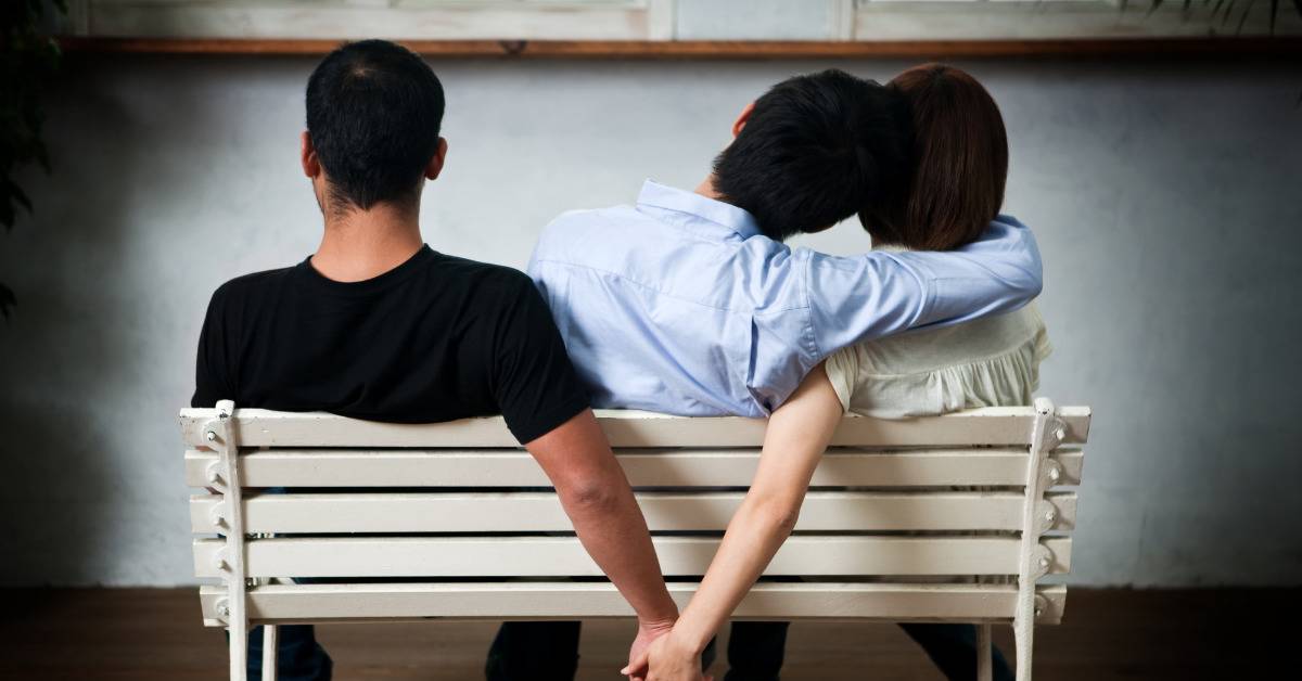 woman and man secretly hold hands on bench