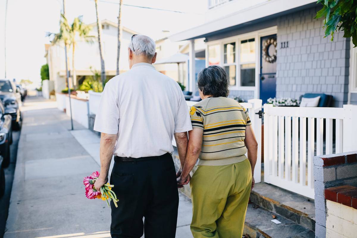 An elderly couple holding hands as they walk down the street.