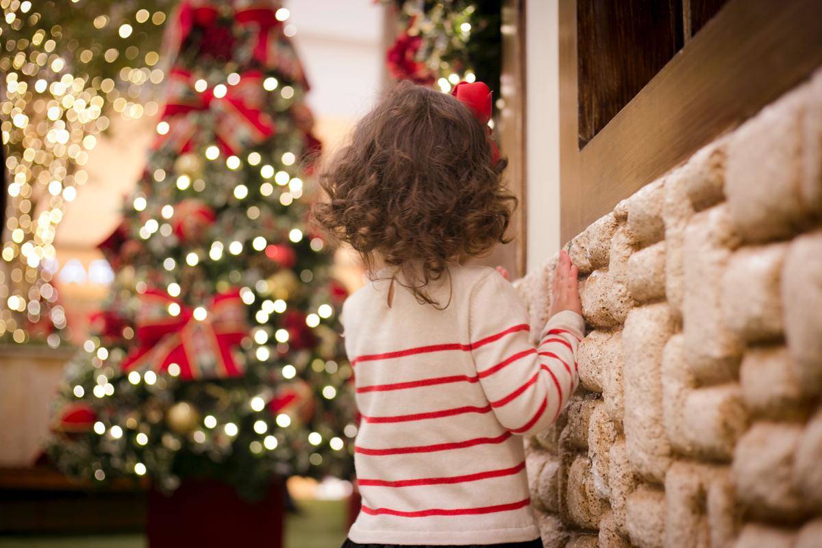A child standing next a wall in their home, looking at their Christmas tree.
